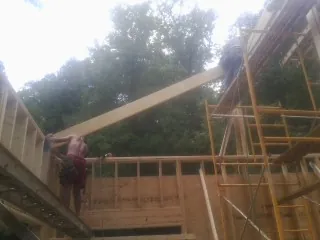 Carpenter raising a rafter beam on a new second story frame in New Concord