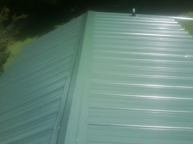 New green metal panels meeting at the ridge of a roof — Flat Roof Repair work by our crew in New Concord