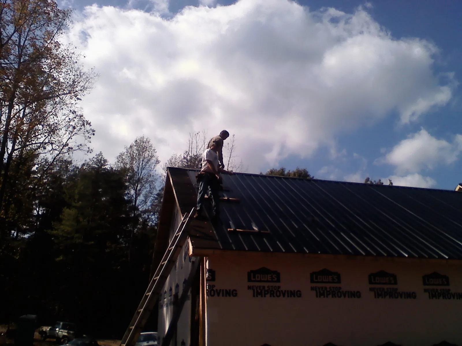 Roofer fastening dark metal panels high against a cloudy sky, from a Roof Inspection job in New Concord
