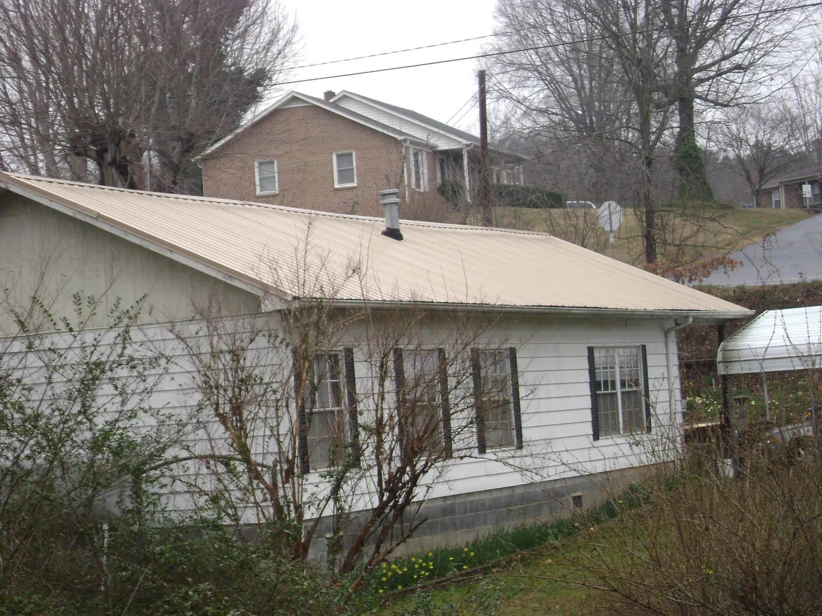 Tan metal roof on a white sided house set into a hillside — Commercial Roofing by Roofing Brothers in New Concord