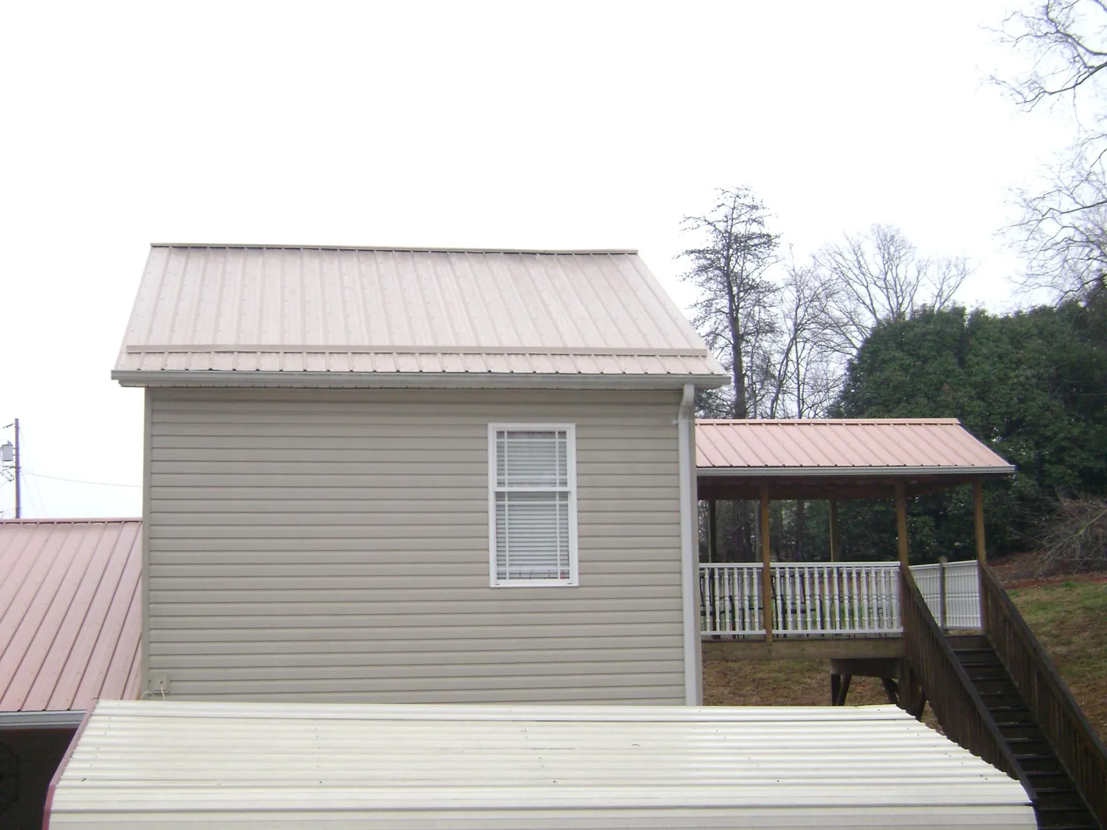 Tan metal roofs on a two story addition and attached porch, from a Roof Replacement job in New Concord